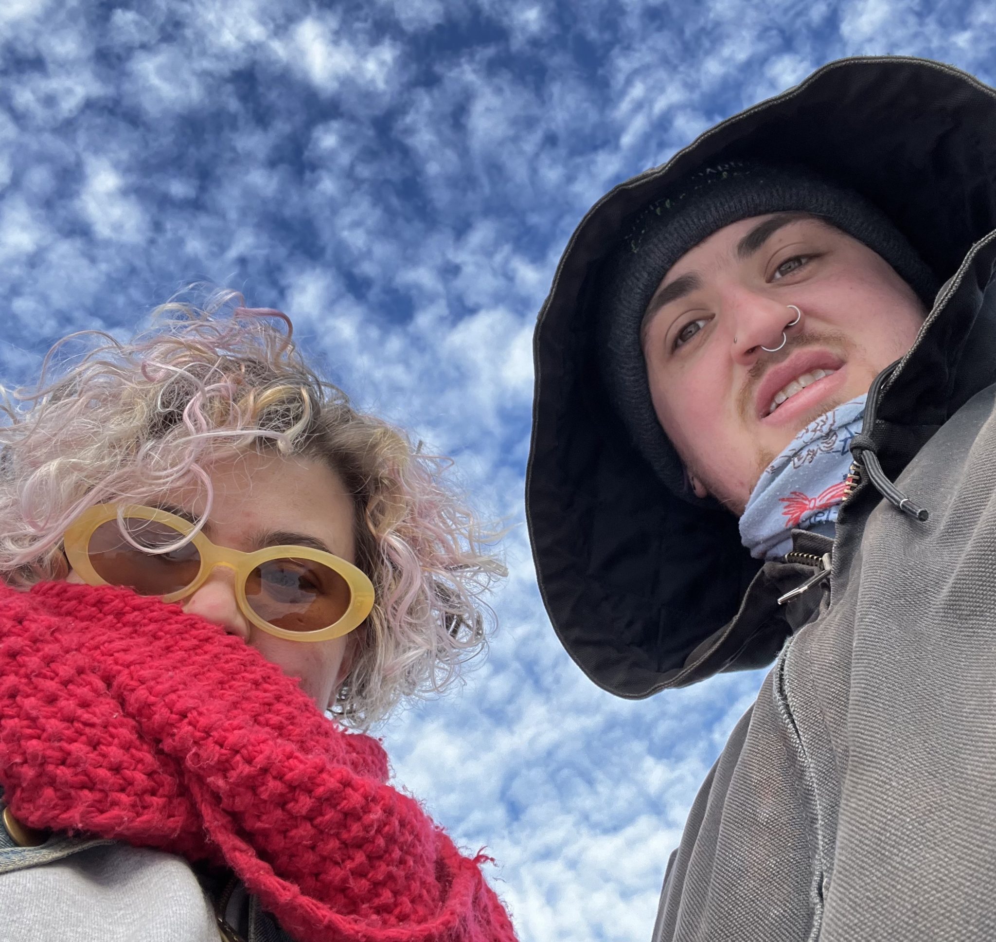 looking up, a photo of two people in winter gear with blue sky and white clouds in the background above them