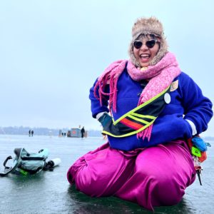 a person wearing heartshaped sunnies and colorful winterwear kneels on the ice