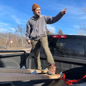 a person stands in the bed of a pickup truck and points in the distance