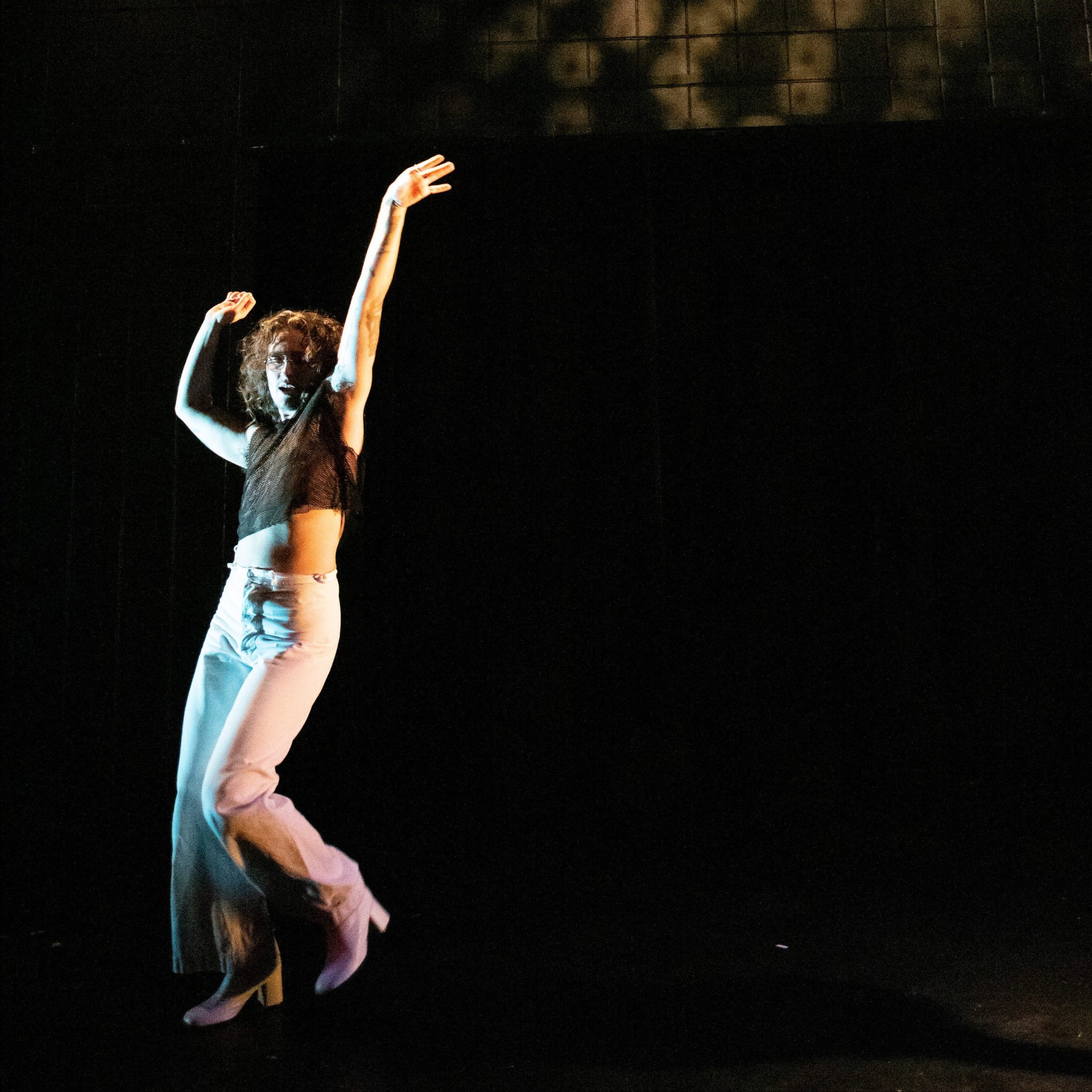 a person wearing a crop top, white pants and gogo boots dances against a black backdrop