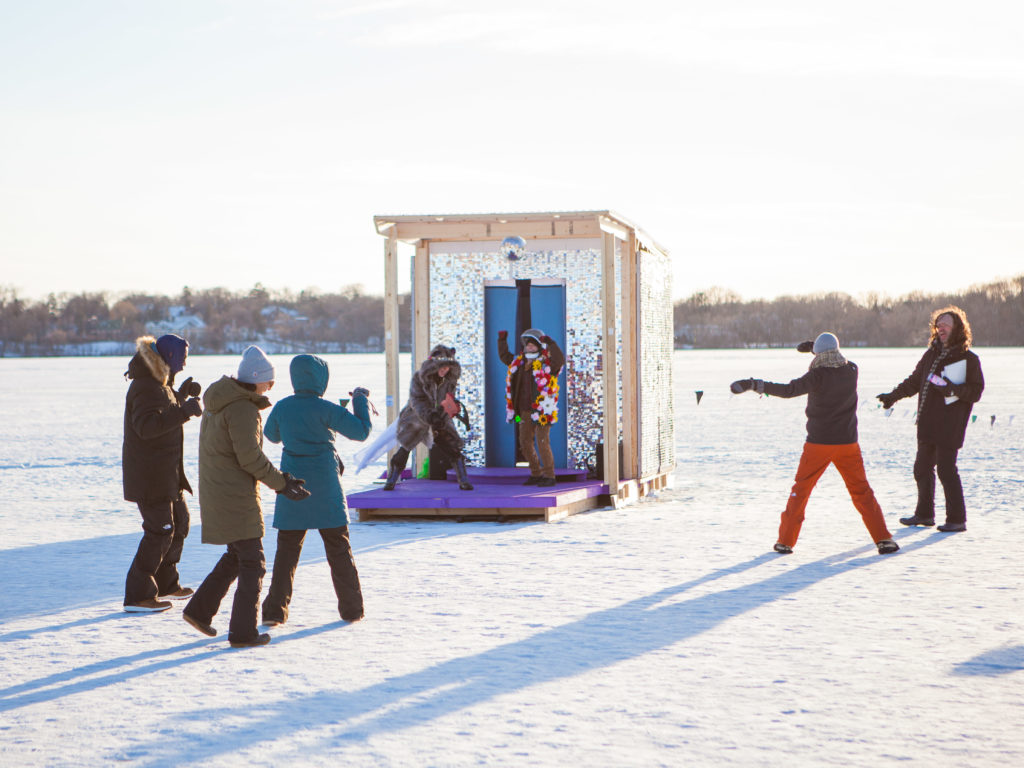 people watch performers in dressup clothing on a shiny stage in the shanty village