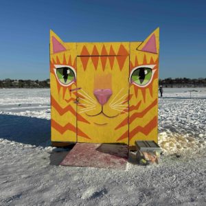 A boxy shanty on a frozen lake painted in bright colors to look like a giant cat face