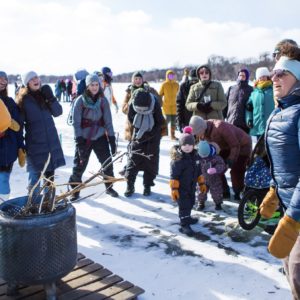 A group of peopel sing around a fire pit on a snowy frozen lake