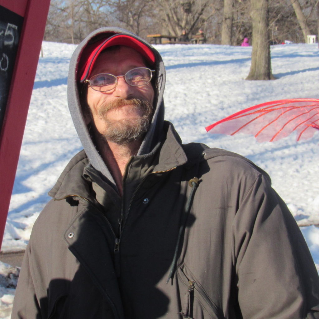 A performer wearing glasses looks up towards the sun against a snowy background