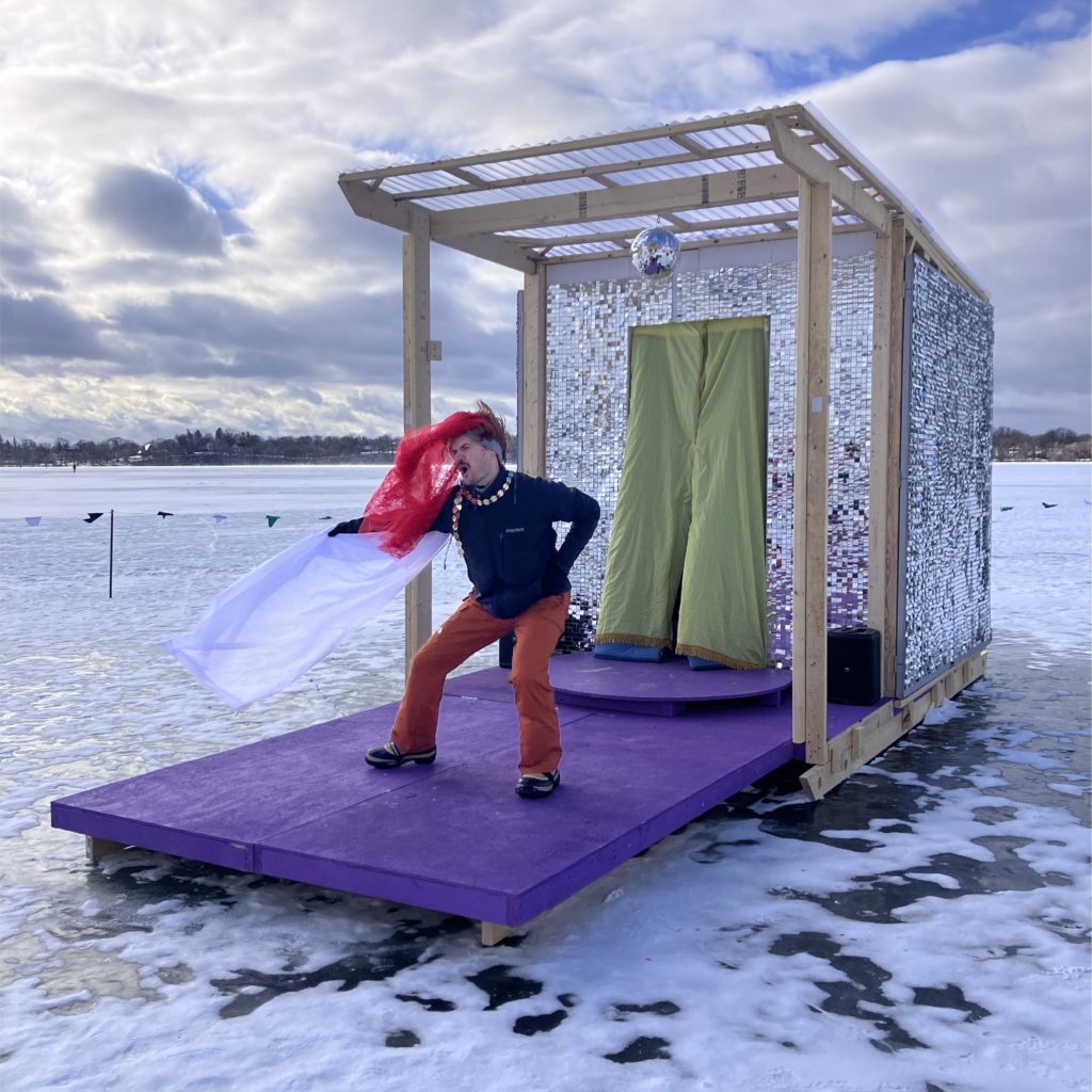 A person performs on a purple platform jutting out from a disco ball inspired shanty