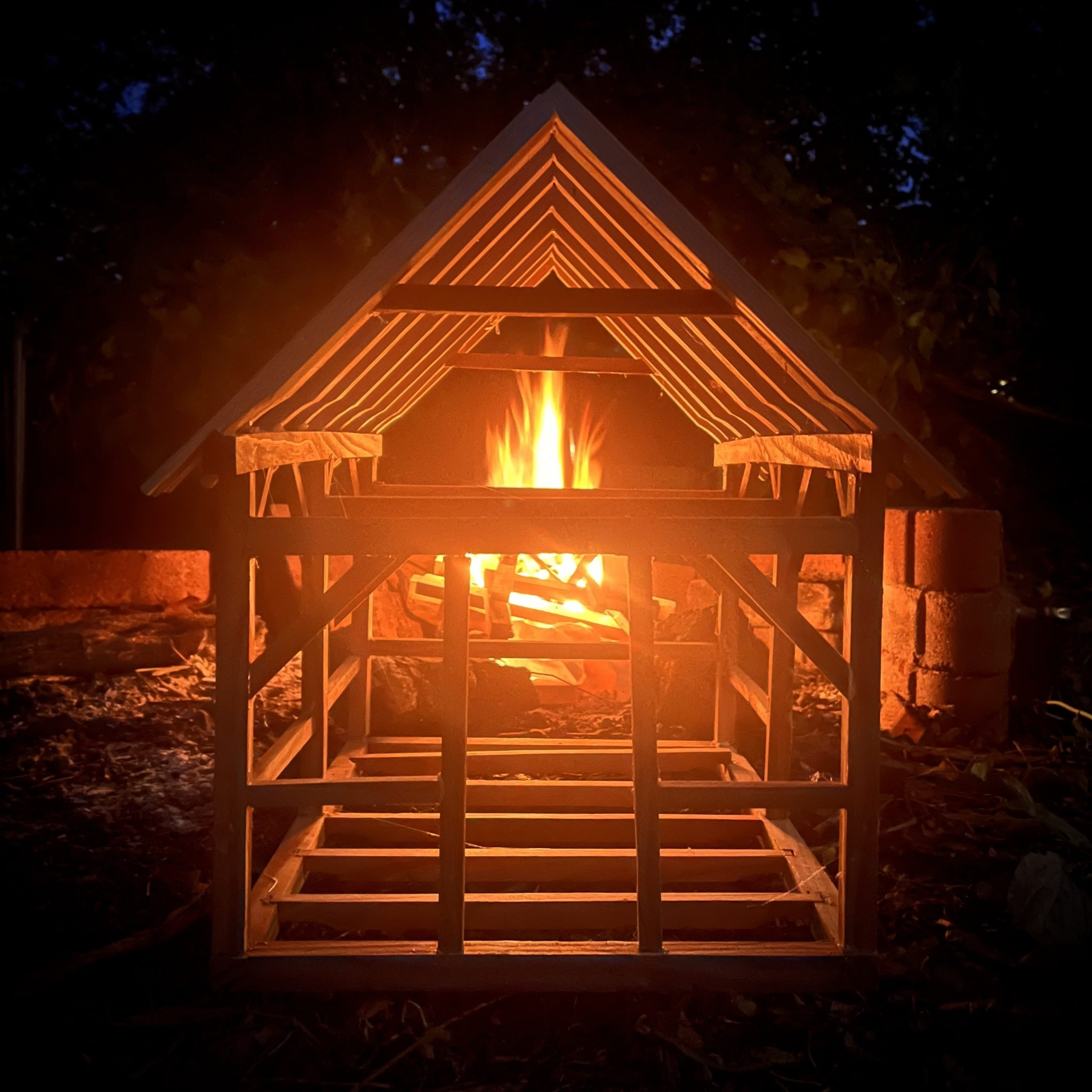 a timber frame structure at night, with a fire burning in the back of it