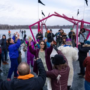 A klezmer band plays on an outdoor shanty stage while visitors dance joyfully on the frozen lake
