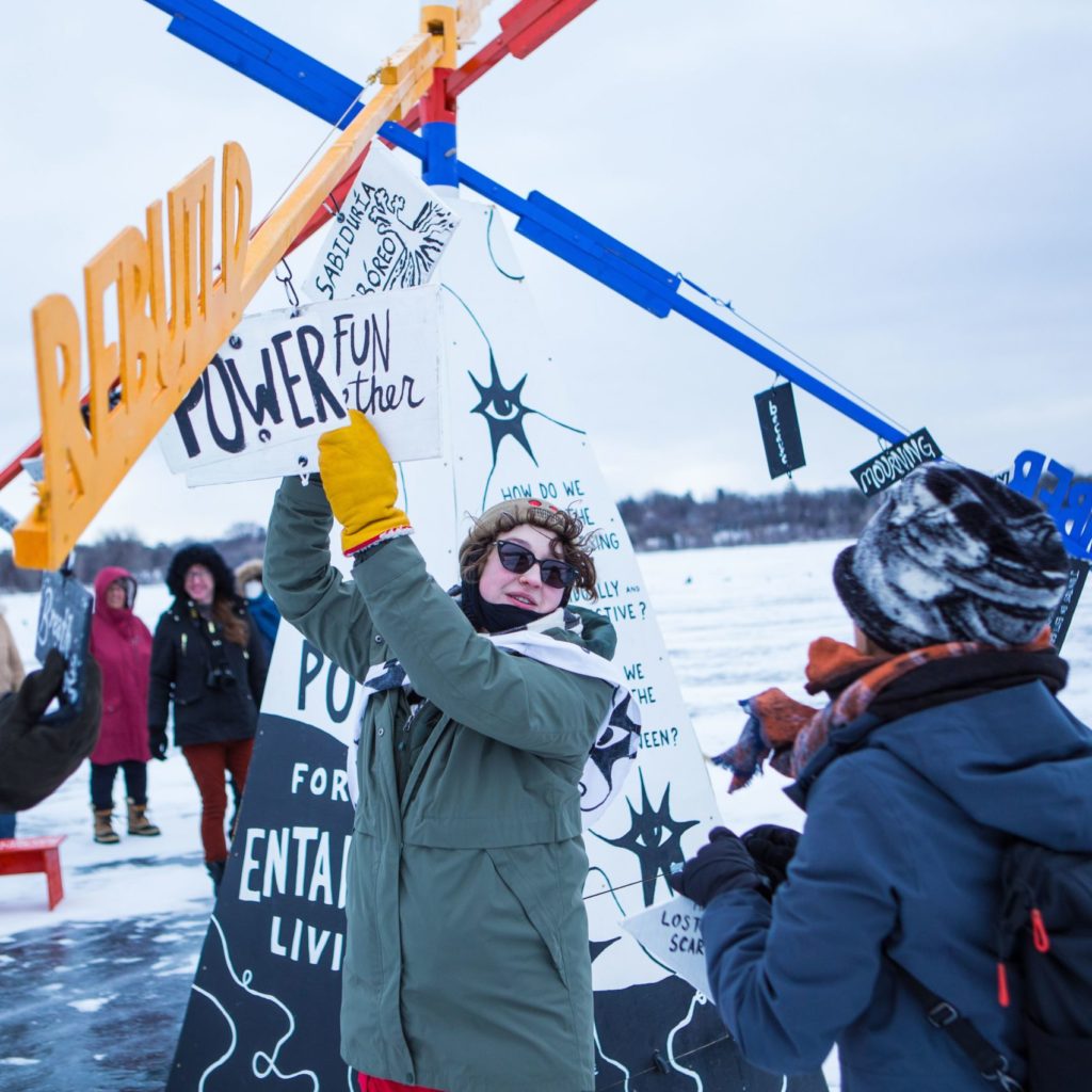 People hang elements to a giant mobile on an arm labeled 'growth'