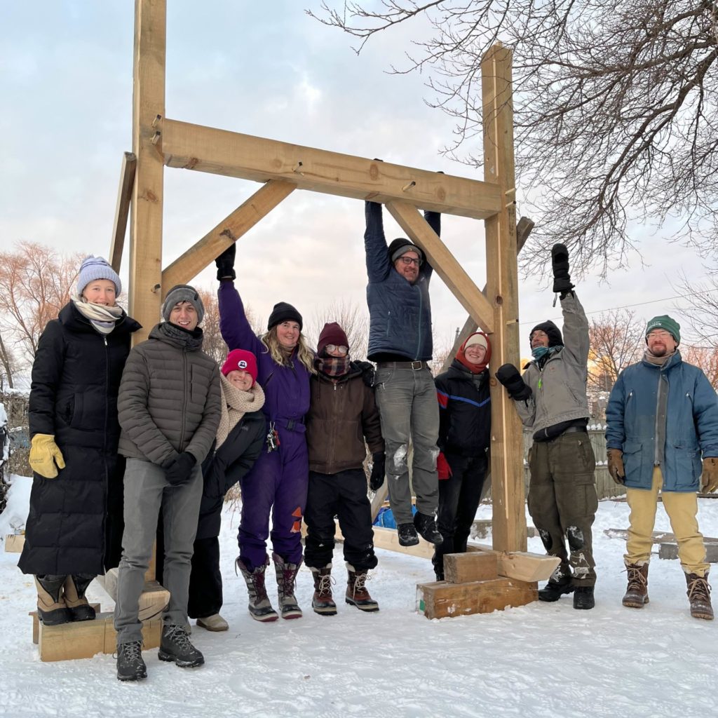 a group poses at an in-progress timber frame structure outside