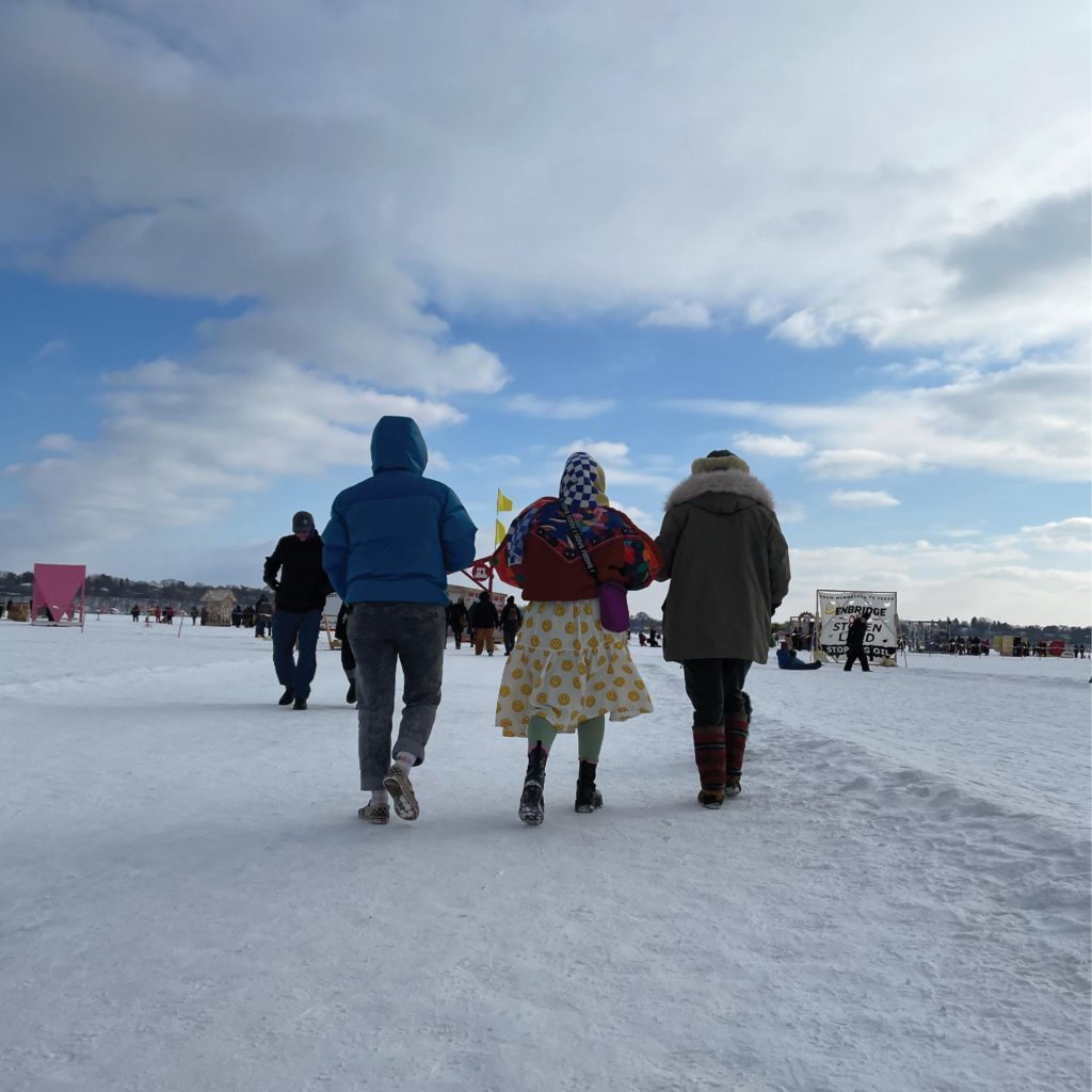 A trio of people, with arms locked, head towards the shanty village