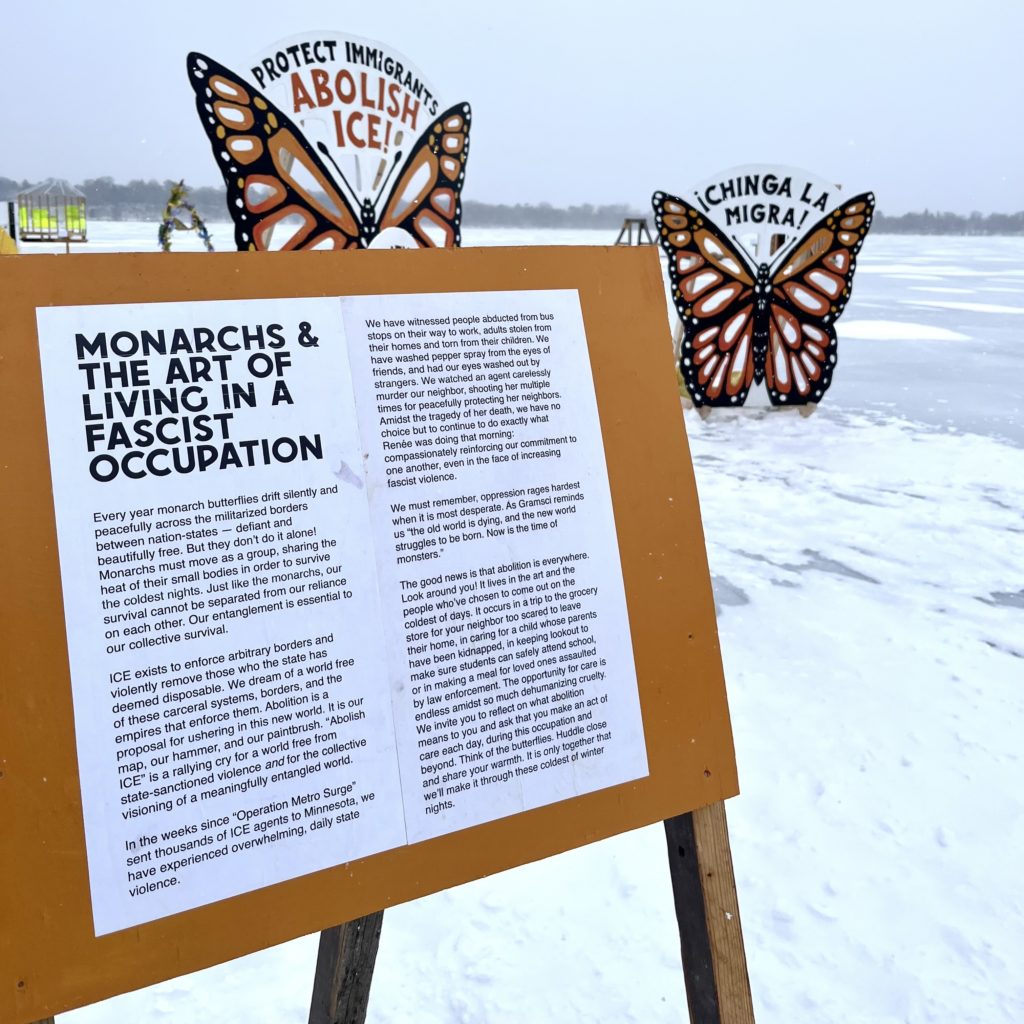 an essay about migration and living under fascism on a sandwich board on the frozen lake with a monarch butterfly installation behind it