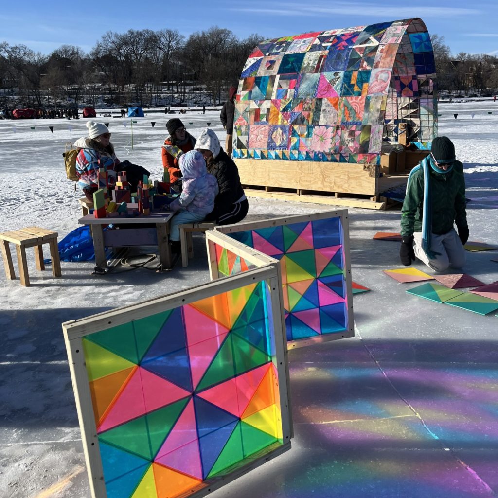 people work on multi-colored puzzles outside of a quilt shanty