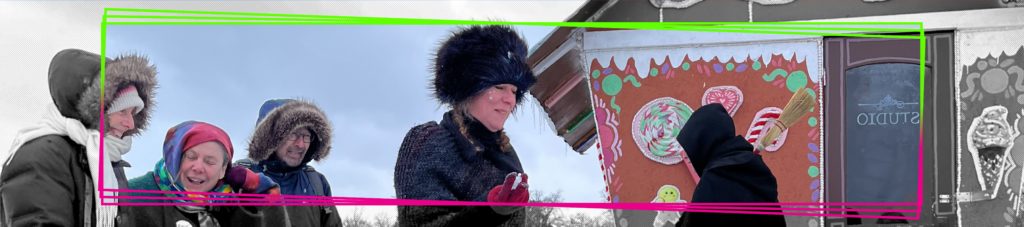 Artists dressed as witches engage with visitors outside their gingerbread house shanty
