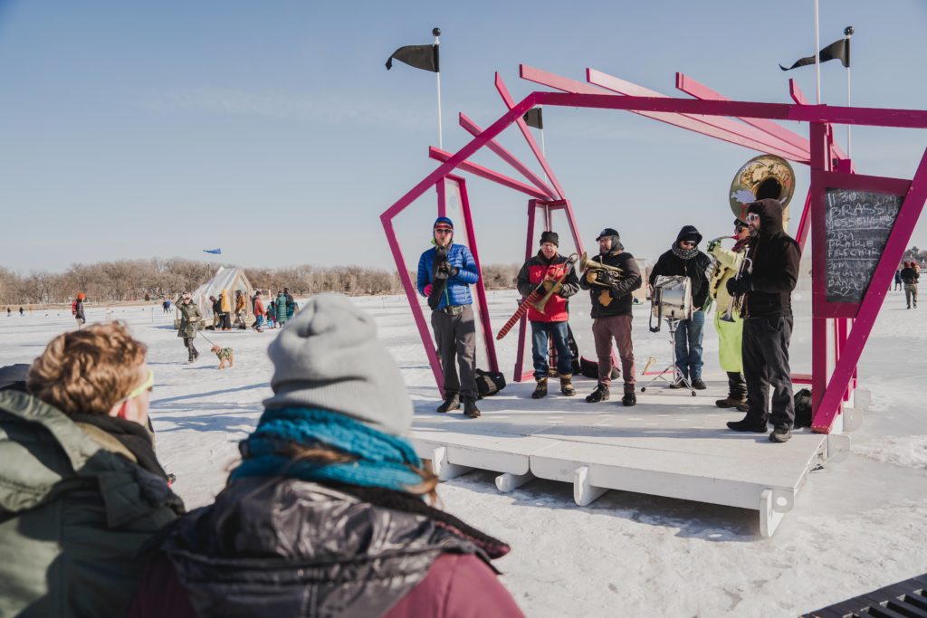 a brass band plays on an outdoor stage in winter on a frozen lake