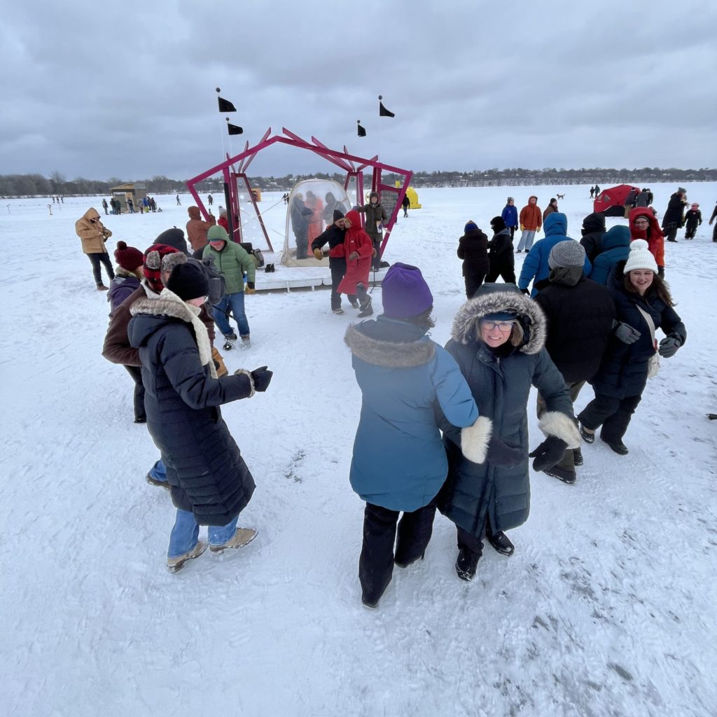 people square dance in snowsuits on a frozen lake