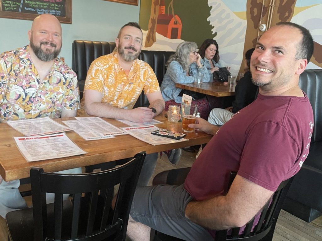 three men at a restaurant table with big smiles