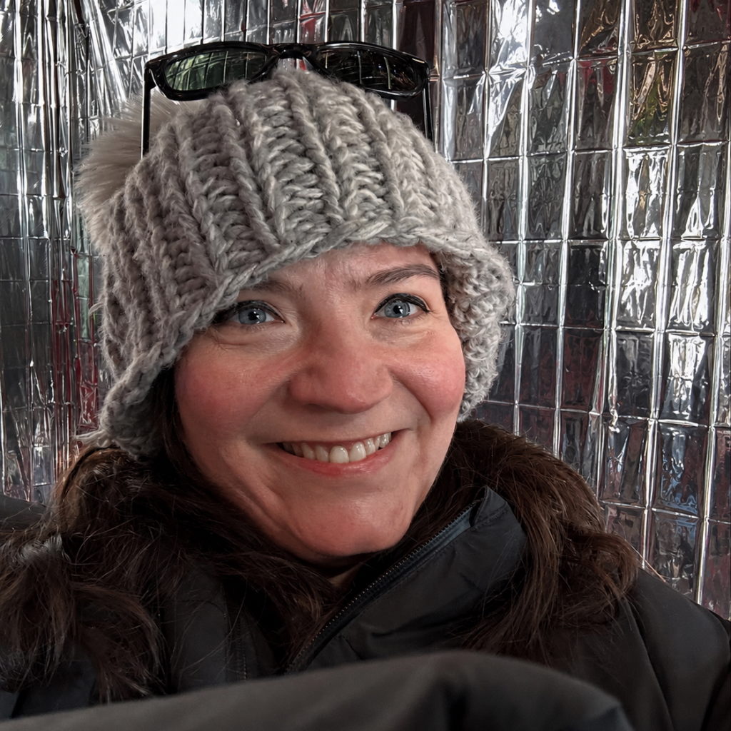 a person wearing a cozy knit hat smiles inside of a shiny shanty