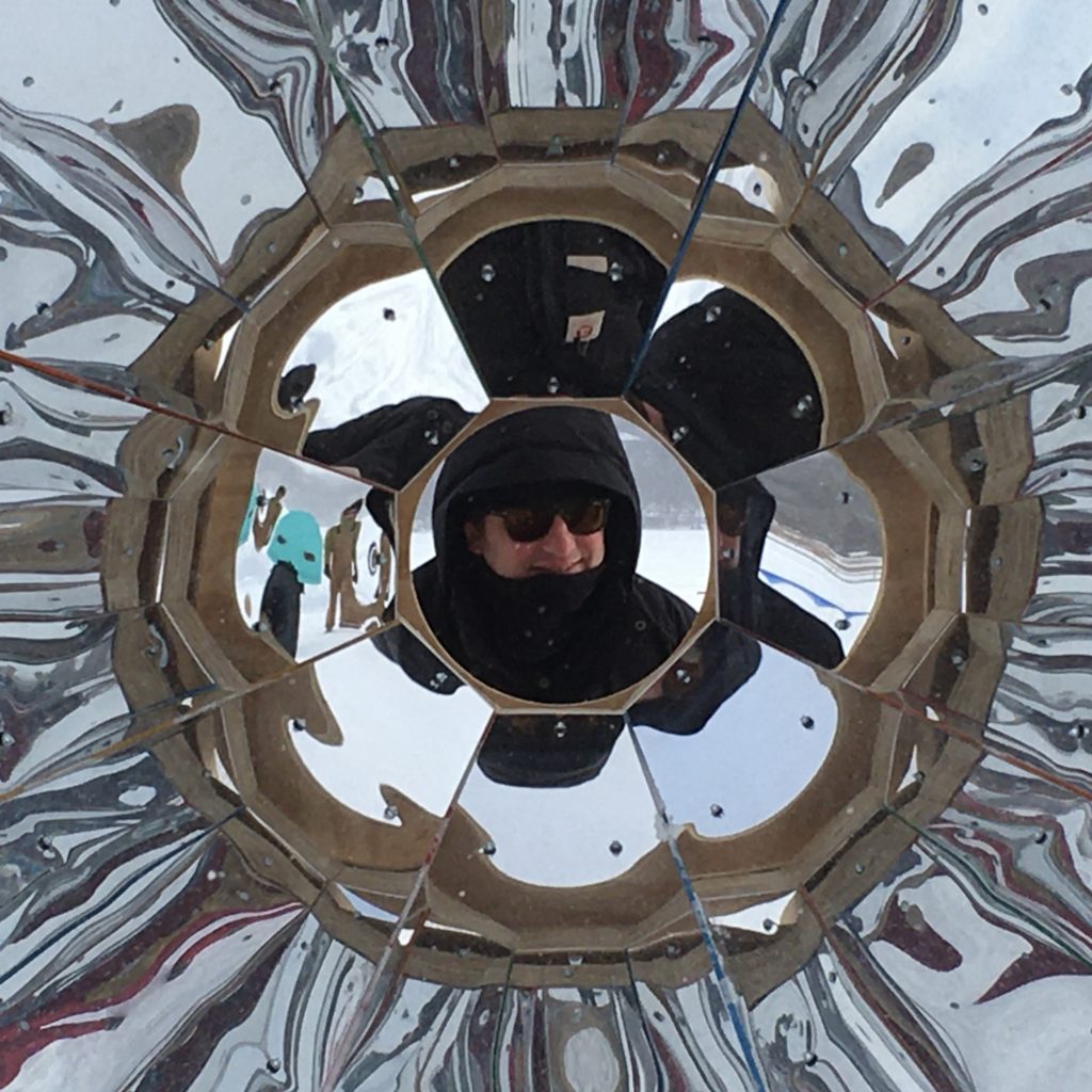a smiling face seen through a giant outdoor shiny kaleidoscope shanty