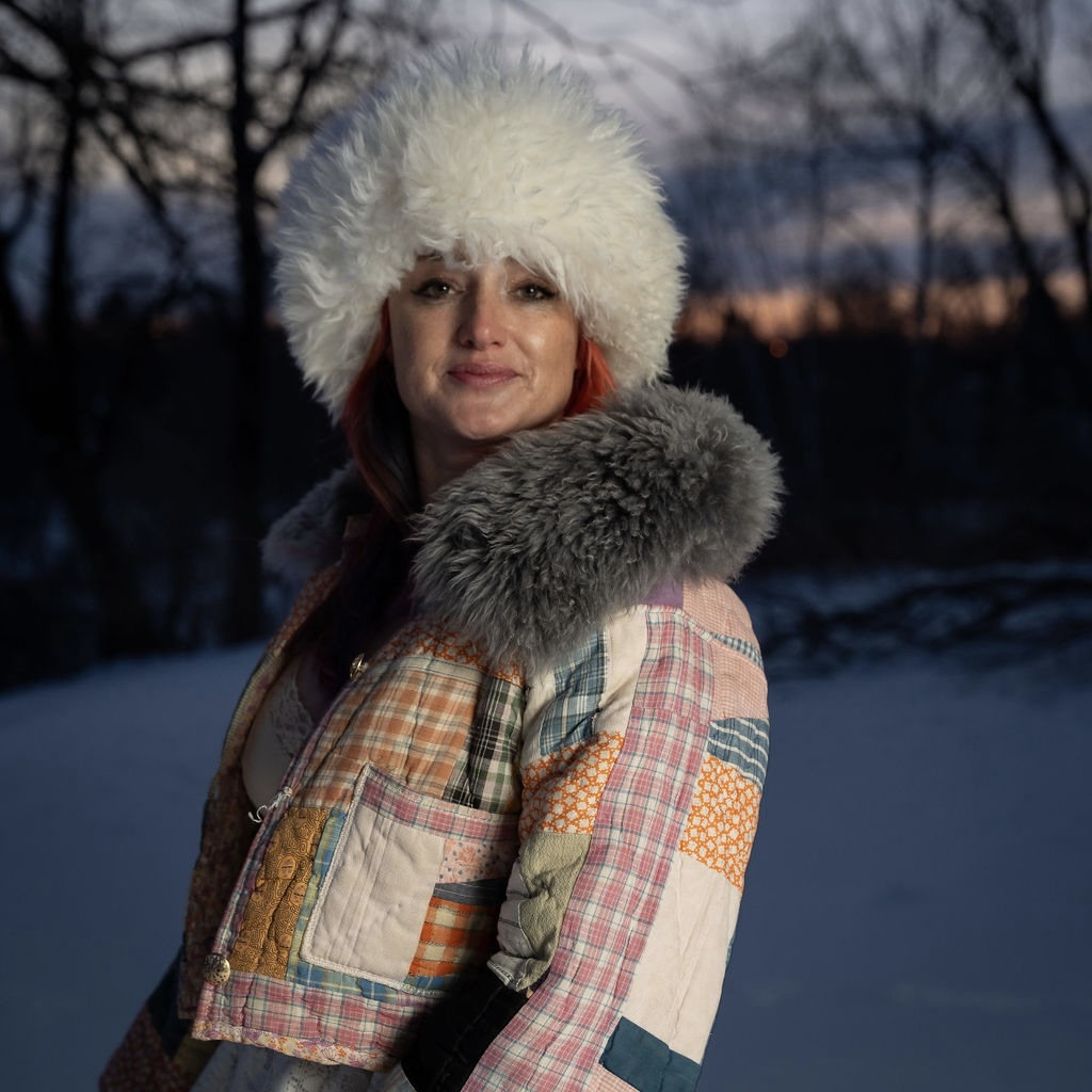 A person wearing a fur hat and patchwork jacket at sunset in winter