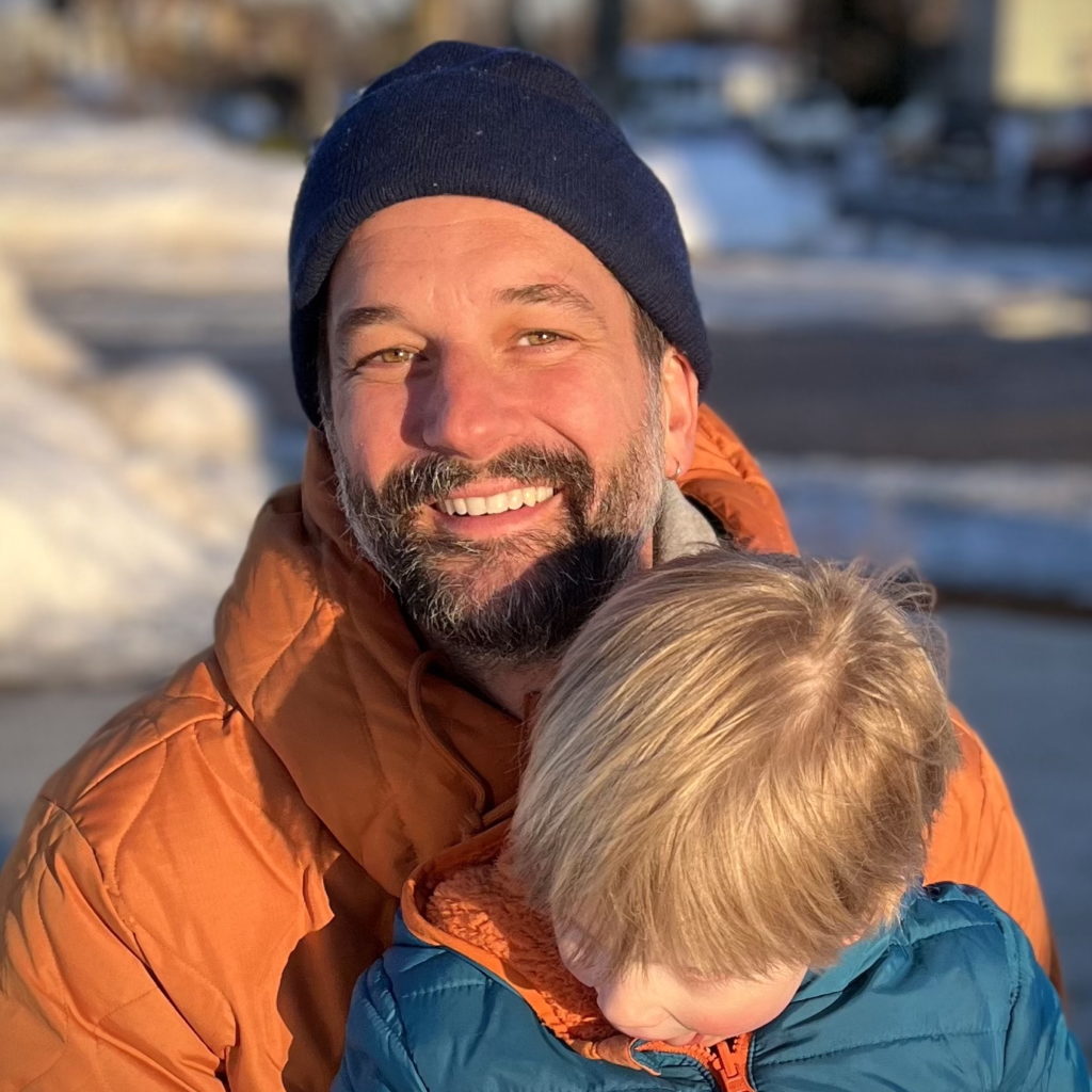 A person wearing an orange coat smiles during golden hour outside in winter
