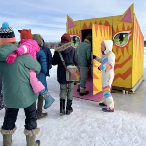 People line up to enter a shanty in the shape of a giant yellow cat head