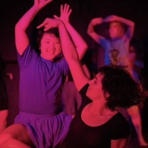 A group of people moving enthusiastically under purple and pink lighting