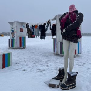 a mannequin in winter fashions with bare legs stands in front of the free store shanty on a snowy day