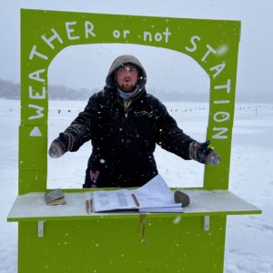 A person stands in a window of a lime green weather station in the snow