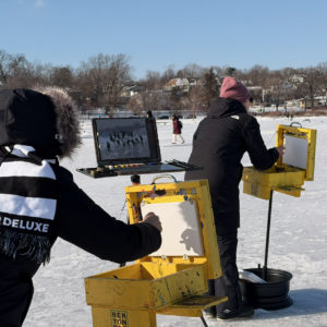 People paint plein air at yellow burton boxes in the shanty village
