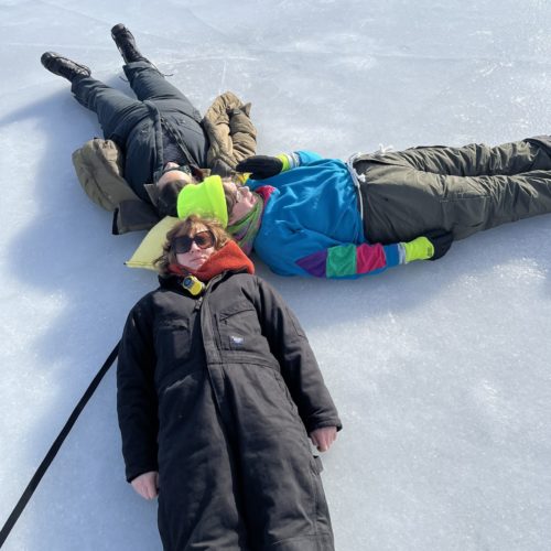 three people lay on the frozen lake, their heads together in the center