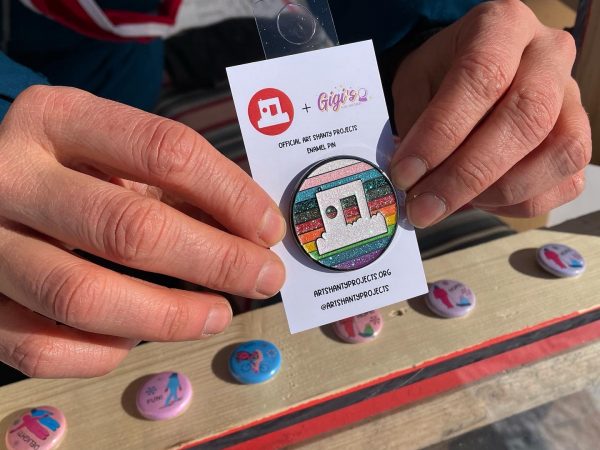 Hands hold a rainbow shanty logo enamel pin