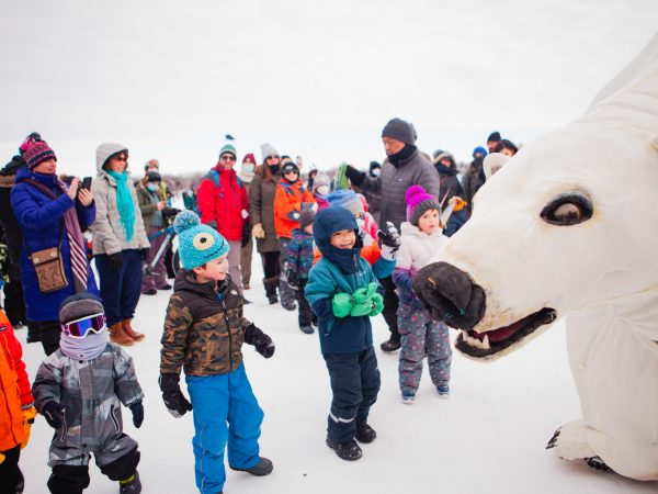 A group of bundled up kiddos look in awe at a giant polar bear puppet